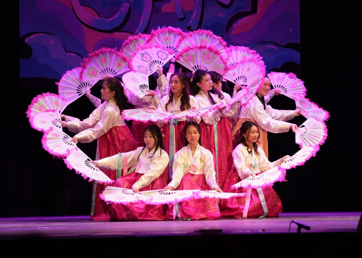 Korean Fan Blooms on Stage—KFan remained one of Cultural Heritage Night’s staple performances due to their consistent visuals and memorable dance. Set in front of the painted Cultural Heritage Mural, the two concentric circles of dancers and their fans form the pistil and petals of a flower.